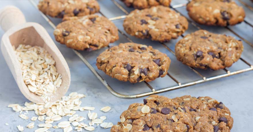 Chocolate chip oat cookies on a rack with oats spilled on the side