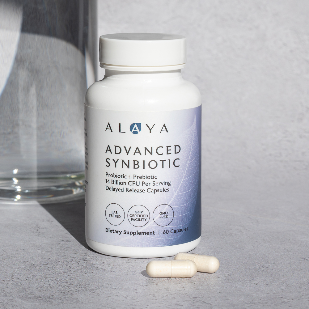 Alaya Advanced Synbiotic supplement bottle on a gray surface with two capsules beside it.